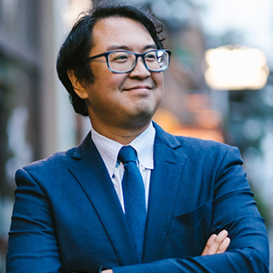 A man in glasses with his arms crossed smiling.