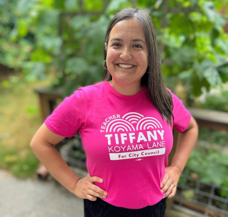 A woman in a pink t-shirt with "Tiffany Koyama Lane for City Council" written on it.